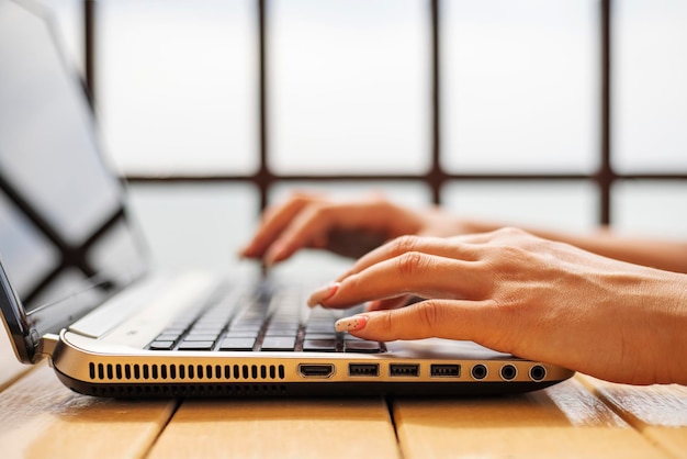 A woman working on laptop at wooden table hands close up