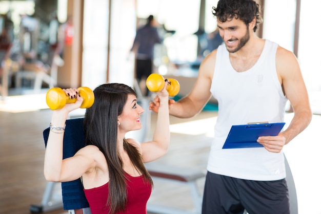 Woman working out in a gym while her personal trainer corrects her posture