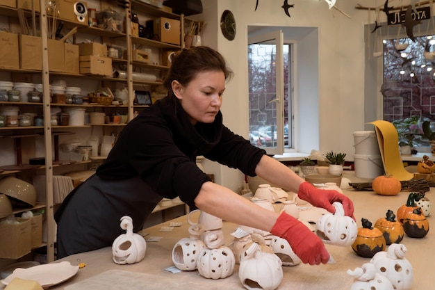 Woman working in pottery workshop making ceramic candle holders with pumpkin shape for Halloween