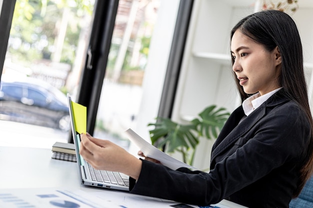 Woman working in a private office, a business woman owner of a company holding a notepad with notes on her laptop, she is checking company financial documents. Concept of company financial management.