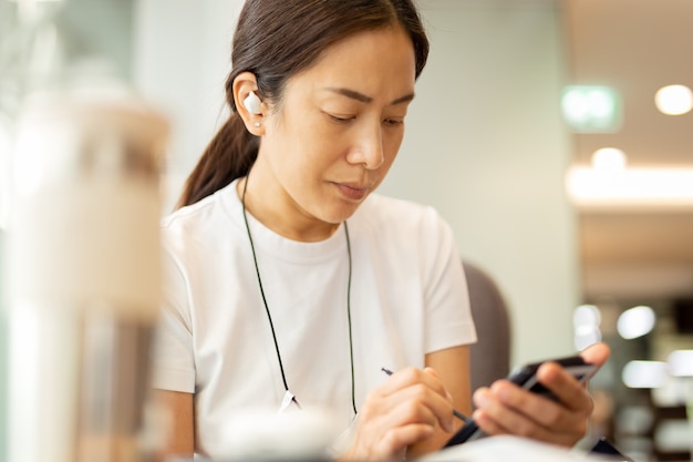 Woman working on smartphone with wireless earphones in cafe.