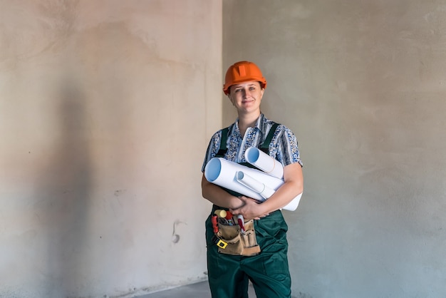 Woman in working uniform with tool belt and blueprints