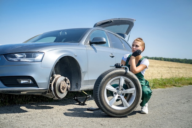 woman working with broken wheel of her car, waiting for help