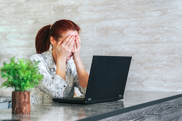 Woman working with laptop feeling sad, frustrated covering face with hands