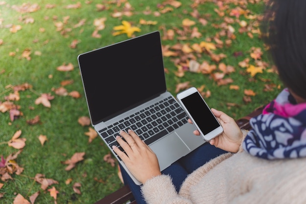 Woman working with smartphone and laptop while sitting in garden.