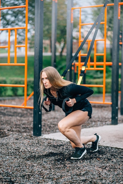 Woman in workout Young athletic female in sportswear trains with fitness straps on sports ground