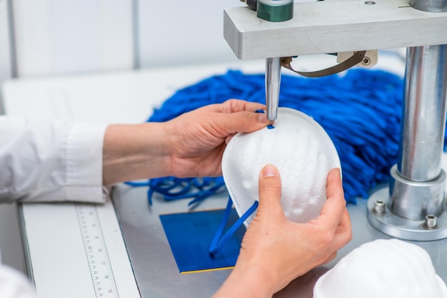 A woman works in a factory for the manufacture of medical masks with nanofibre and solder loops with ultrasound on a machine Coronavirus and Covid19 Protection Closeup