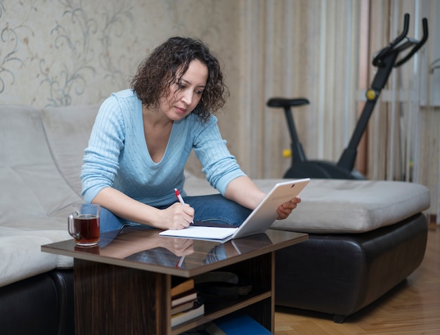 A woman works at home behind a tablet.