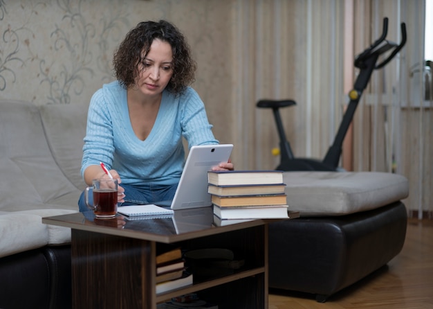 A woman works at home behind a tablet.