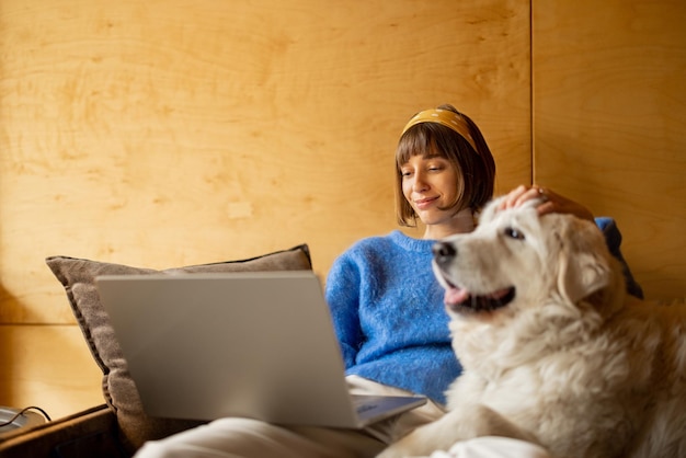 Woman works on laptop while sitting on a couch with her dog