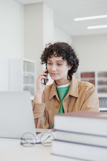 Woman works in library coworking at laptop and talks on phone researcher at university