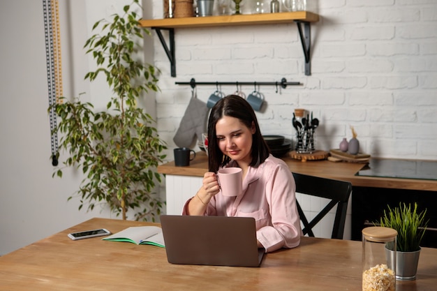 A woman works in the office remotely from home in the kitchen, sitting at the computer. Distance learning online education and work. Girl student prepares for exams.