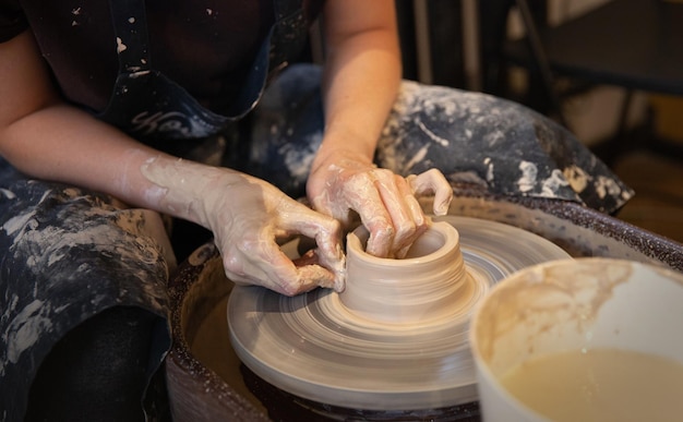 A woman works on a potter's wheel Hands form a cup of wet clay on a potter's wheel Artistic concept