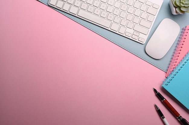 Woman workspace with keyboard, notebook and pen on pink table.