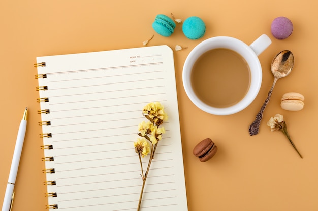 Woman workspace with macaroons, flowers, notebook and coffee cup