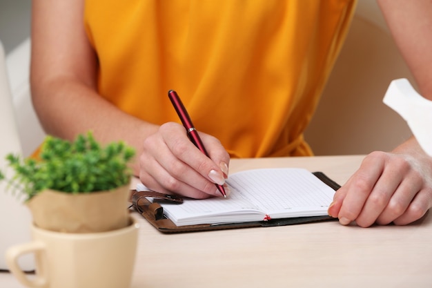 Woman write on notebook on workplace close up