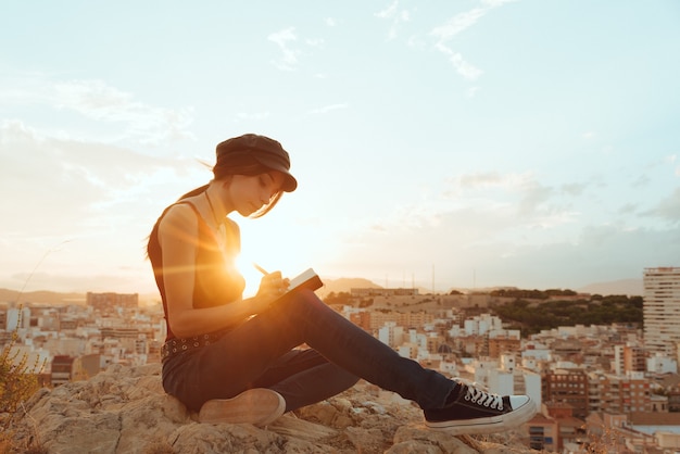 Woman writes in her note book phrases and thoughts outdoors at sunset