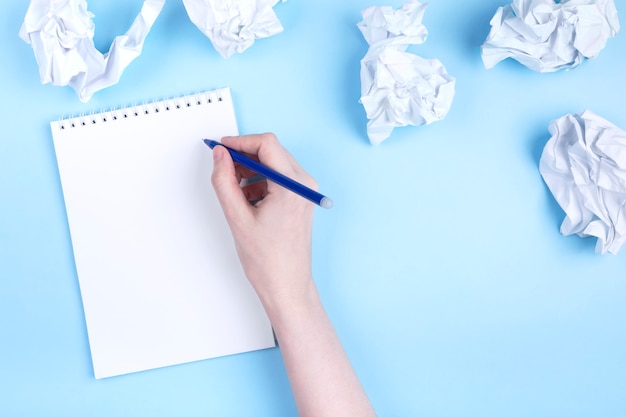 Woman writes in notebook around crumpled paper, blue background