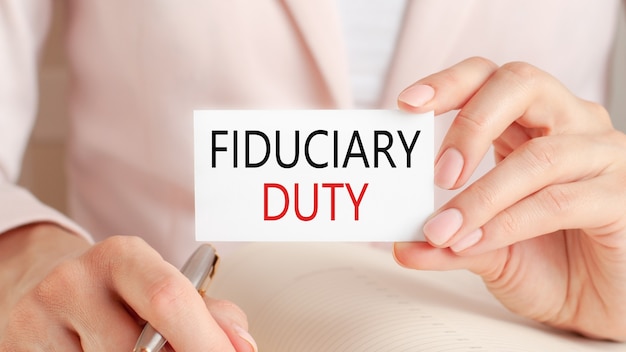 Woman writes in a notebook with a silver pen and hand hold white paper card with text: fiduciary duty