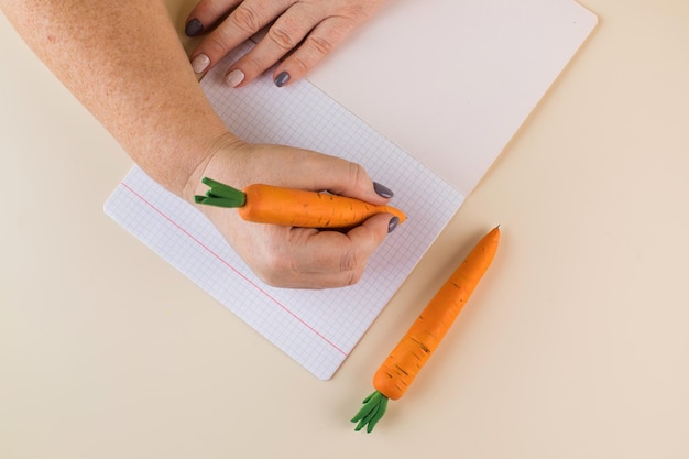 Woman writes with pen in handmade carrot shaped casing at beige table upper view