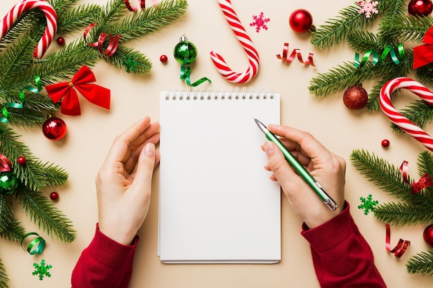 Woman writing Christmas to do list on notebook on colored background with xmas decorations