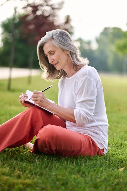 Woman writing in notebook on grass in park