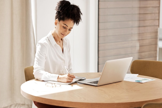 Woman writing in notebook laptop on table and home office of accountant auditor or financial advisor Finance report strategy and budget planning black woman doing research on tax audit documents