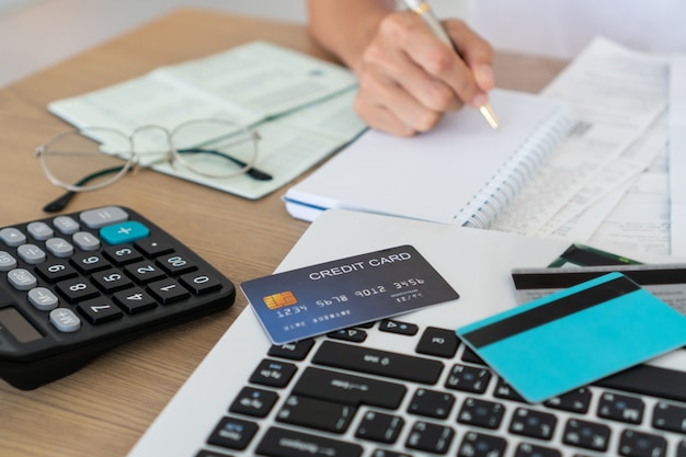 Woman writing on notebook with computer, calculator and credit card on desk, account and saving concept.