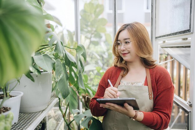 a woman writing in a notebook with a pen and a plant in the background