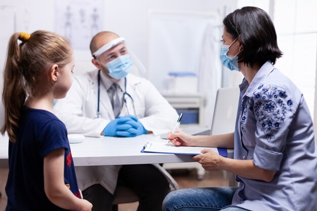 Woman writing prescription on clipboard listening doctor instructions. Health pediatrician specialist providing health care services consultations treatment in protective equipment for consultation