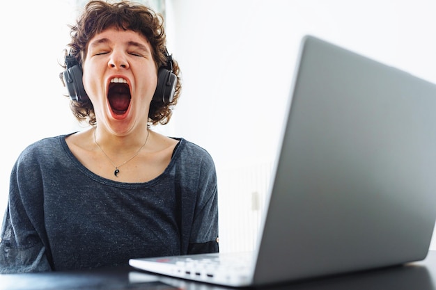 A woman yawns in front of a laptop with a laptop open.