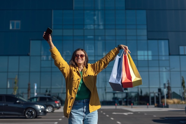 Woman in yellow jacket holding smartphone and shopping bag with a groceries in hands