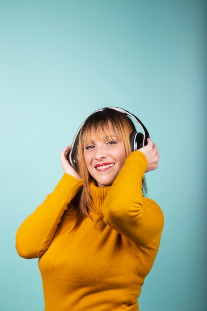 Woman in yellow pullover smiling towards camera with headphones listening to music  Isolated image.