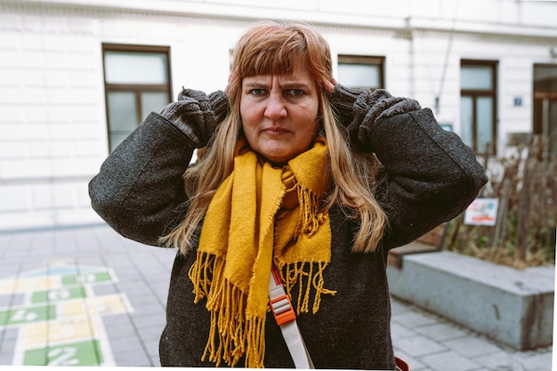 A woman in a yellow scarf stands in front of a white building.