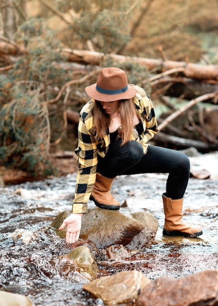 Woman in yellow shirt and hat sitting on the river bank in the autumn forest