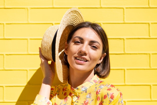 Woman in yellow summer dress and hat on yellow brick wall calm and positive, enjoys sunny summer days