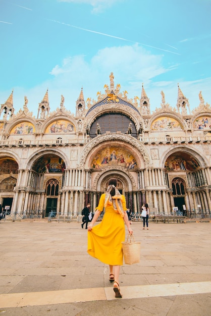 Woman in yellow sundress with straw hat walking to saint mark basilica