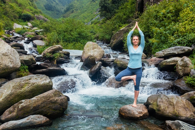 Woman in yoga asana Vrikshasana tree pose at waterfall outdoors