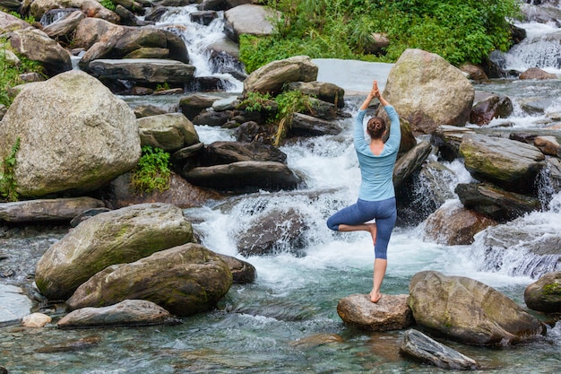 Woman in yoga asana Vrikshasana tree pose at waterfall outdoors