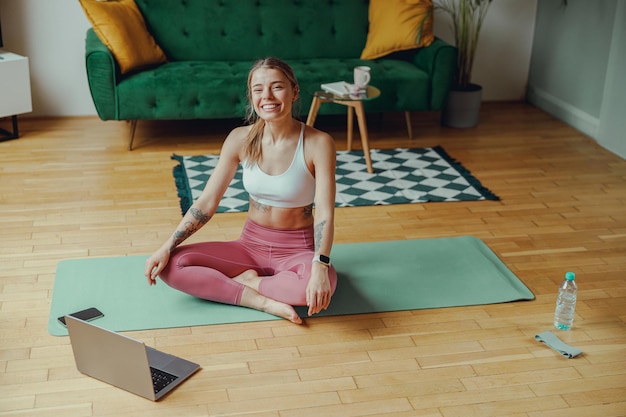 Woman on yoga mat facing laptop on hardwood floor finding comfort in leisure