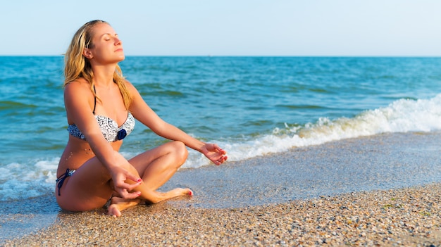 Woman in yoga pose sitting by sea