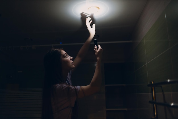 Woman young holding hand flashlight in darkness Disconnecting home electricity and changing lamp bulb