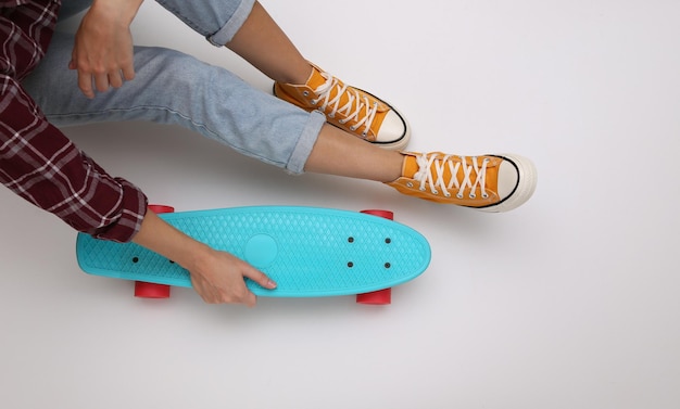 Woman in youth clothing holds cruiser board on white background. Top view