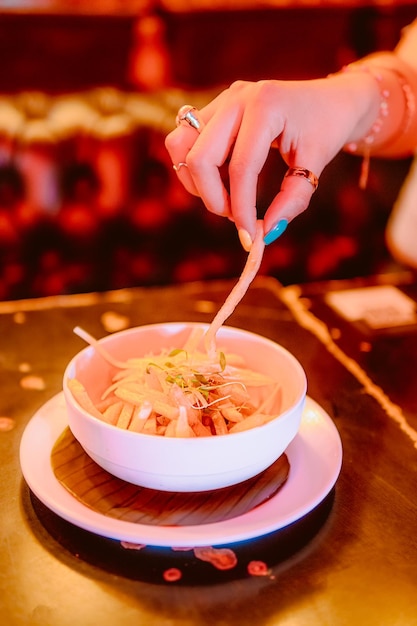 A woman39s hand holds a French fry from a plate of potatoes a tasty snack to eat at the restaurant