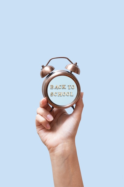 A woman39s hand is holding an alarm clock with the inscription Back to school