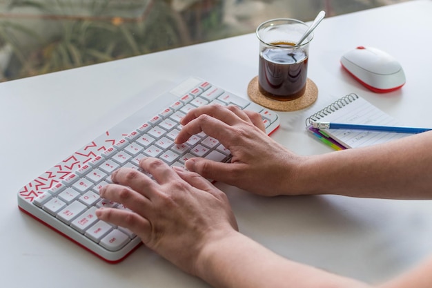 Woman39s hand typing on a white keyboard with red letters with coffee in the background On white table