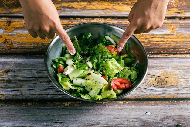 Woman39s hands pointing to a bowl of salad on a wooden table Healthy food