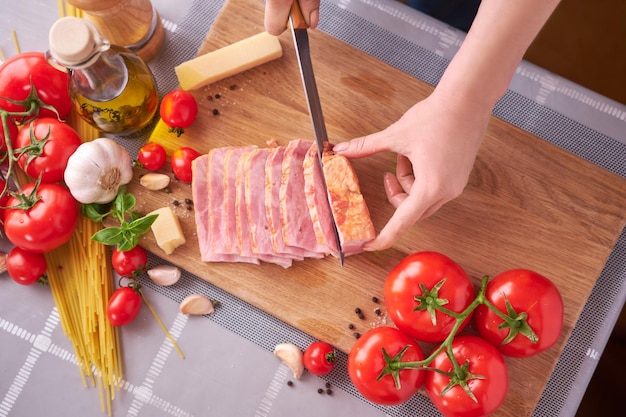 Woman39s hands slicing pancetta ham bacon on wooden cutting board at domestic kitchen