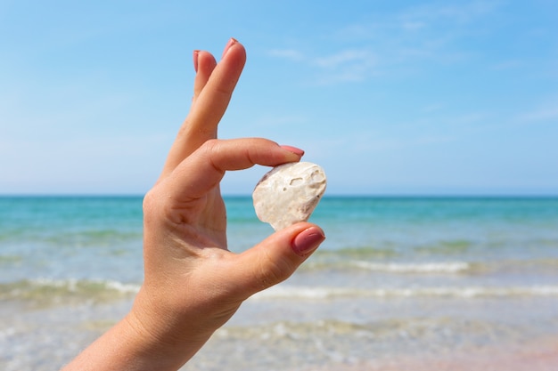 Womana´s hand holding a seashell on the beach.