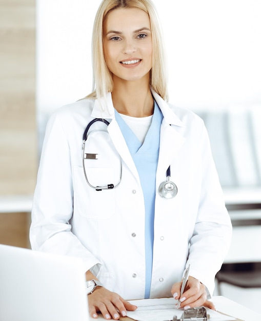 Womandoctor at work in clinic happy of her profession Blond female physician controls medication history record and medical exam results Medicine concept